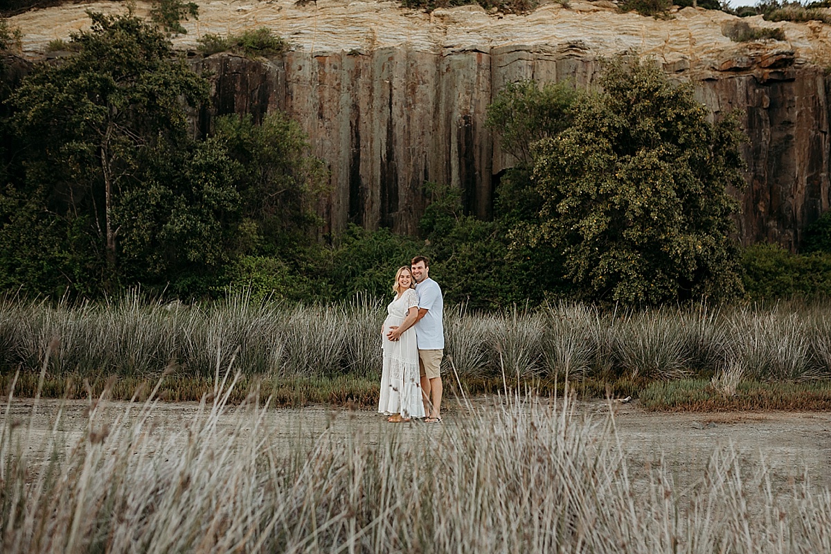 Couple standing in front of cliff face at maternity session