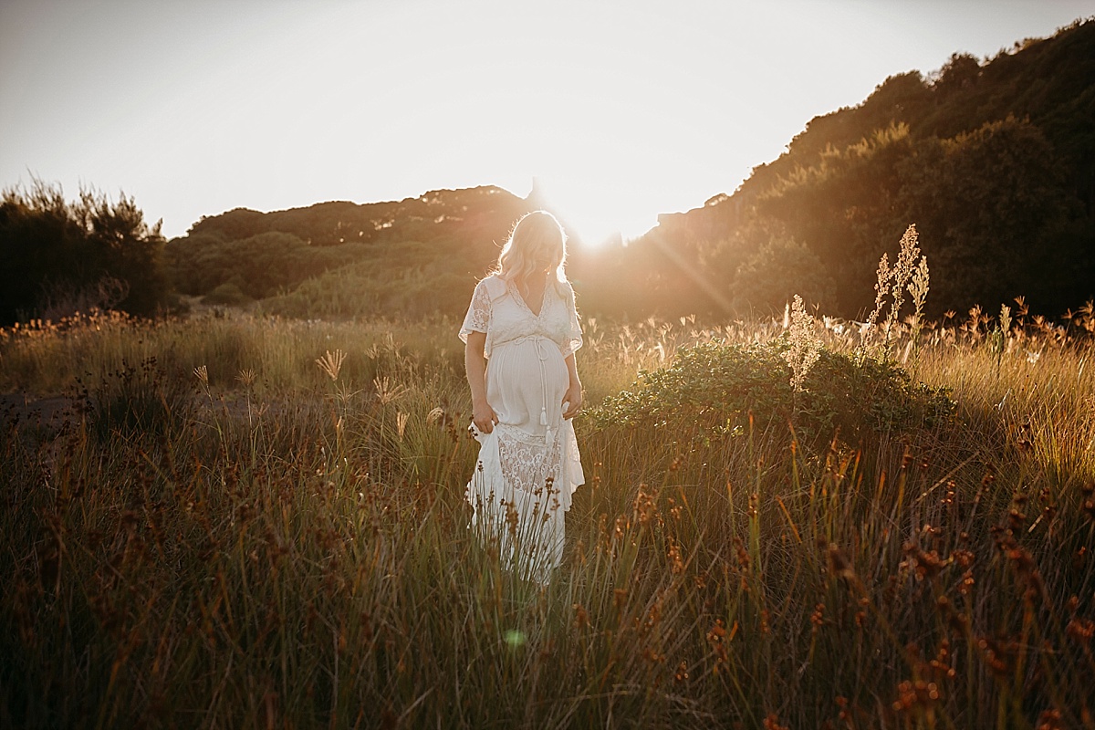 Pregnant mum walking through grass holding dress at sunset