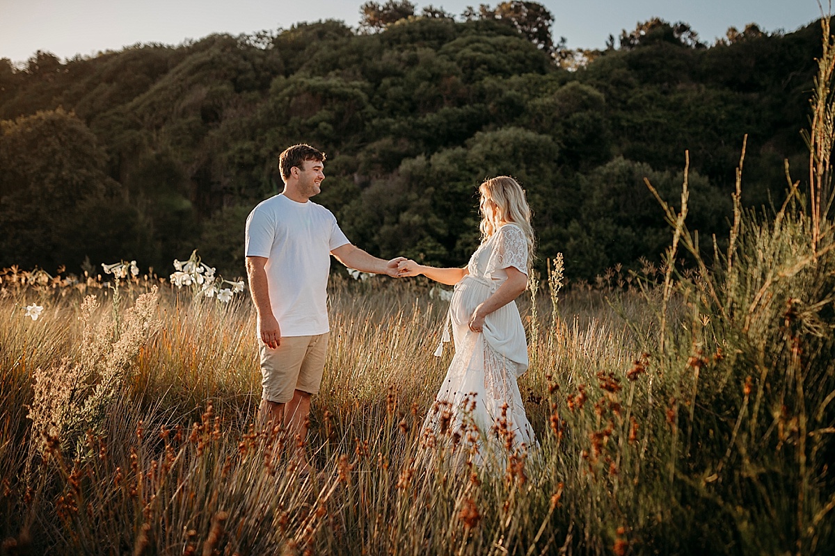 Pregnant mum dancing with husband in long reeds at sunset