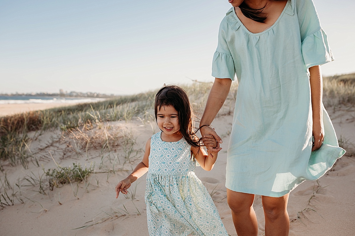 Mother and daughter walking on beach holding hands
