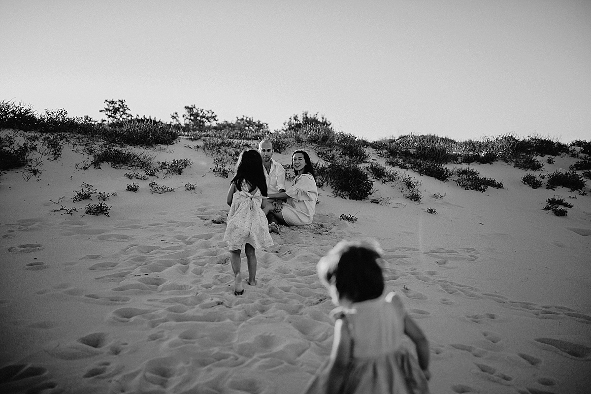 Little girls running to mum and dad sitting on the beach