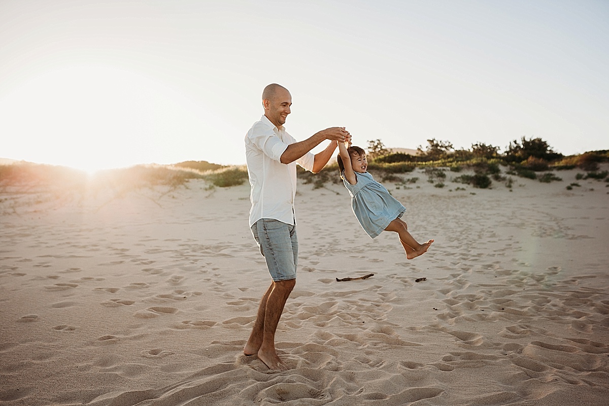 Dad spinning little girl around in the air on beach