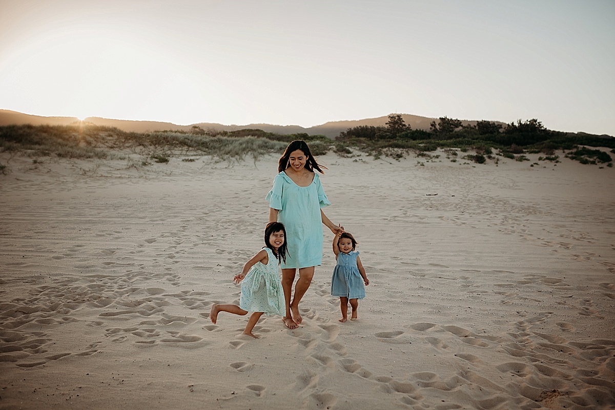 mum and her two daughters walking along beach hand in hand