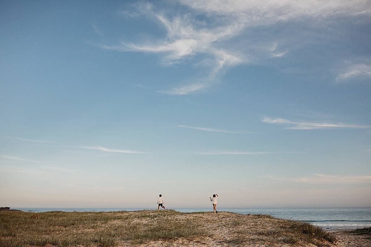 Two boys running on top of sand dune in the distance.