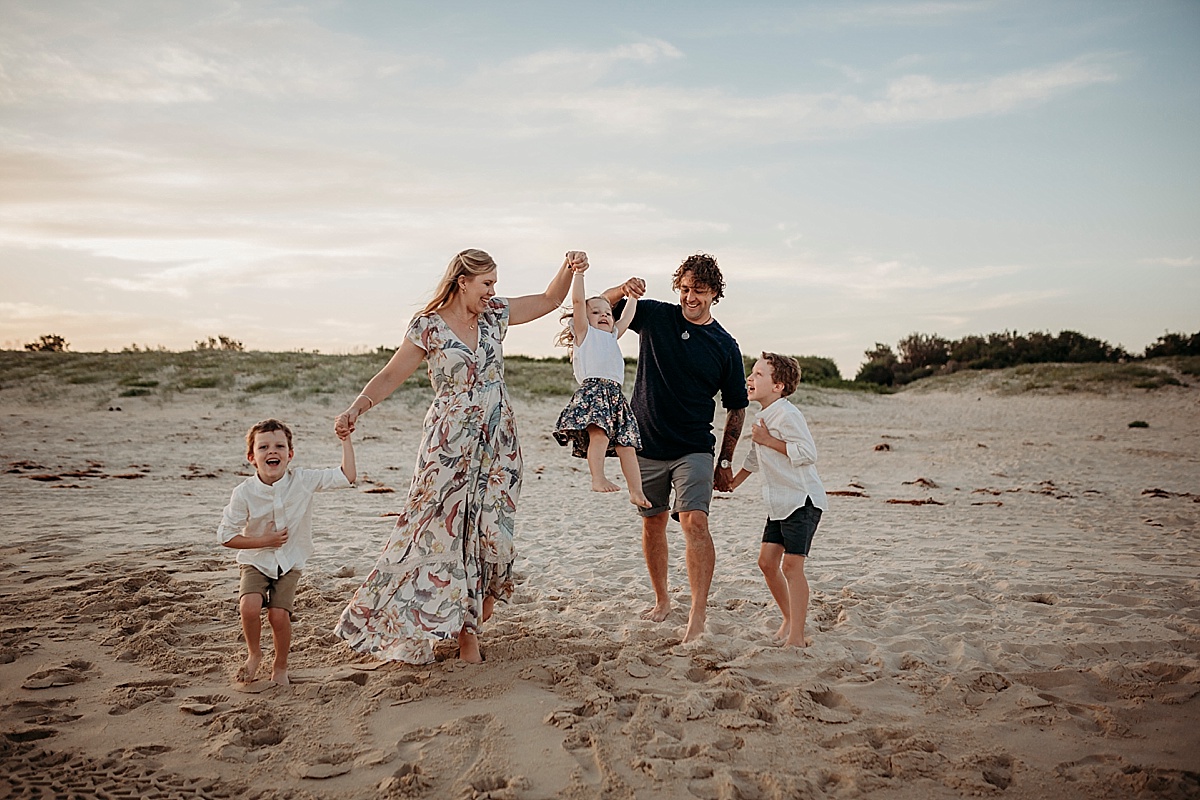 family holding hands walking along beach swinging little girls in air