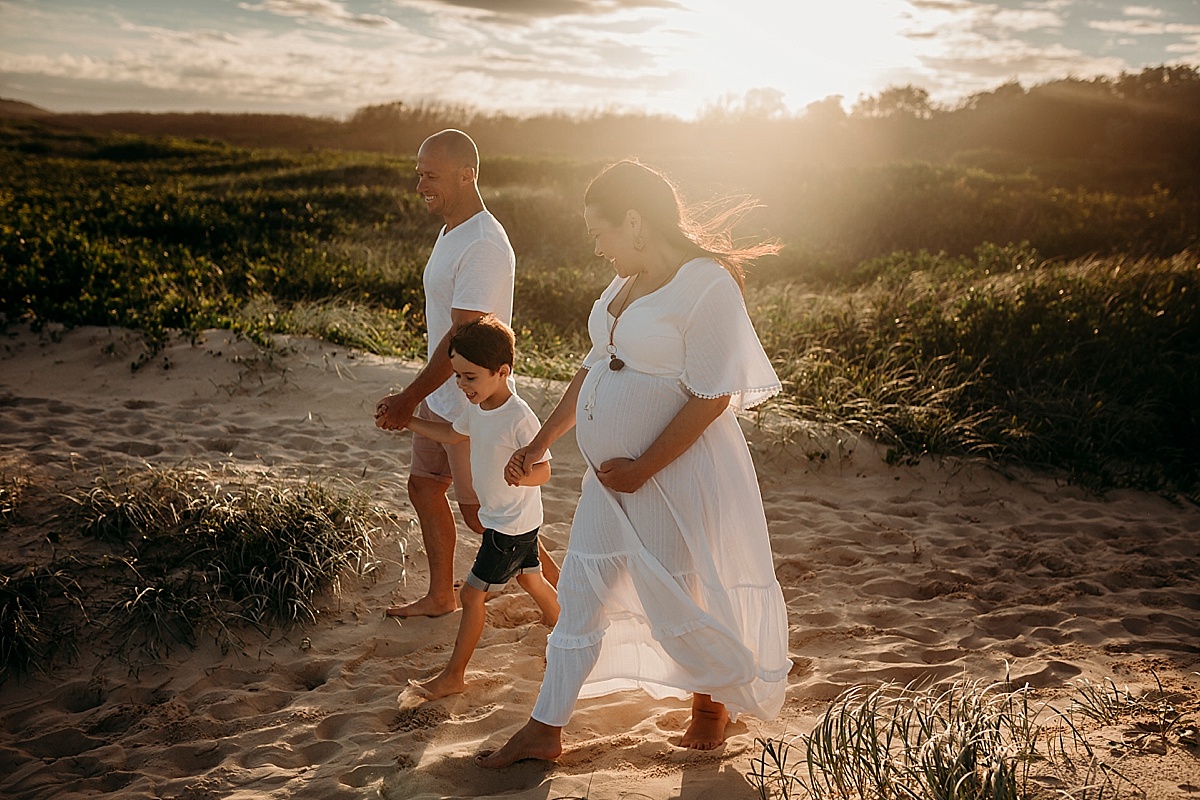 Pregnant mum, son and husband walking down to the beach at sunset