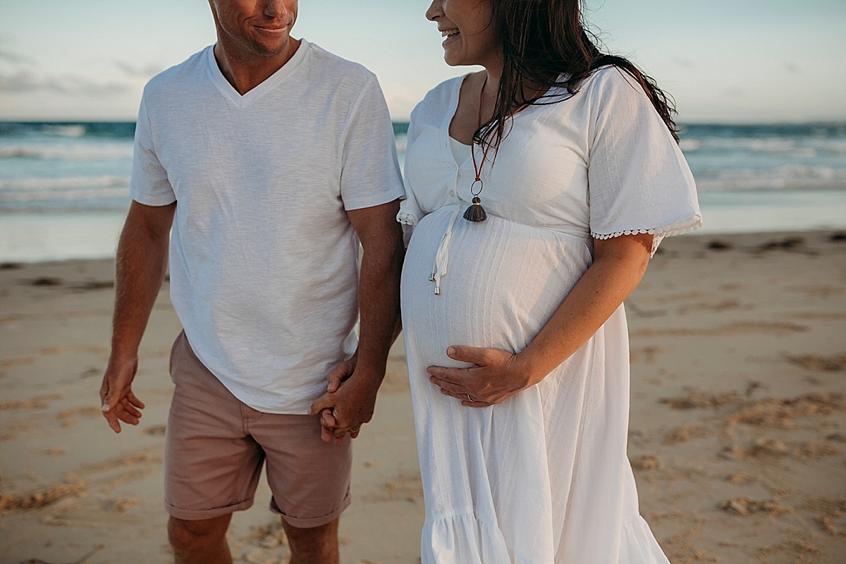 Husband wife holding hands at beach and wife holding pregnant belly