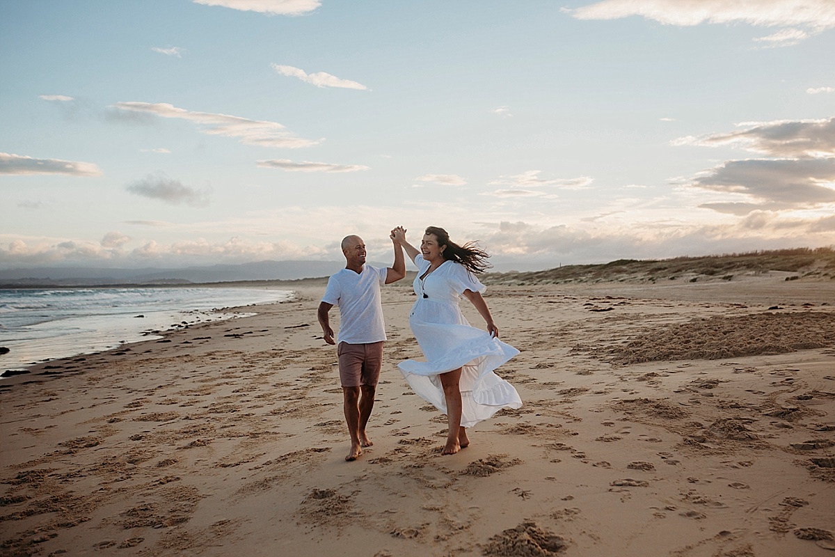 Husband twirling pregnant wife on beach at sunset