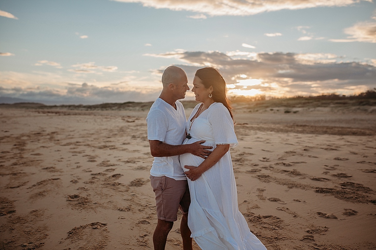 mum and dad and pregnant belly, cuddling at beach