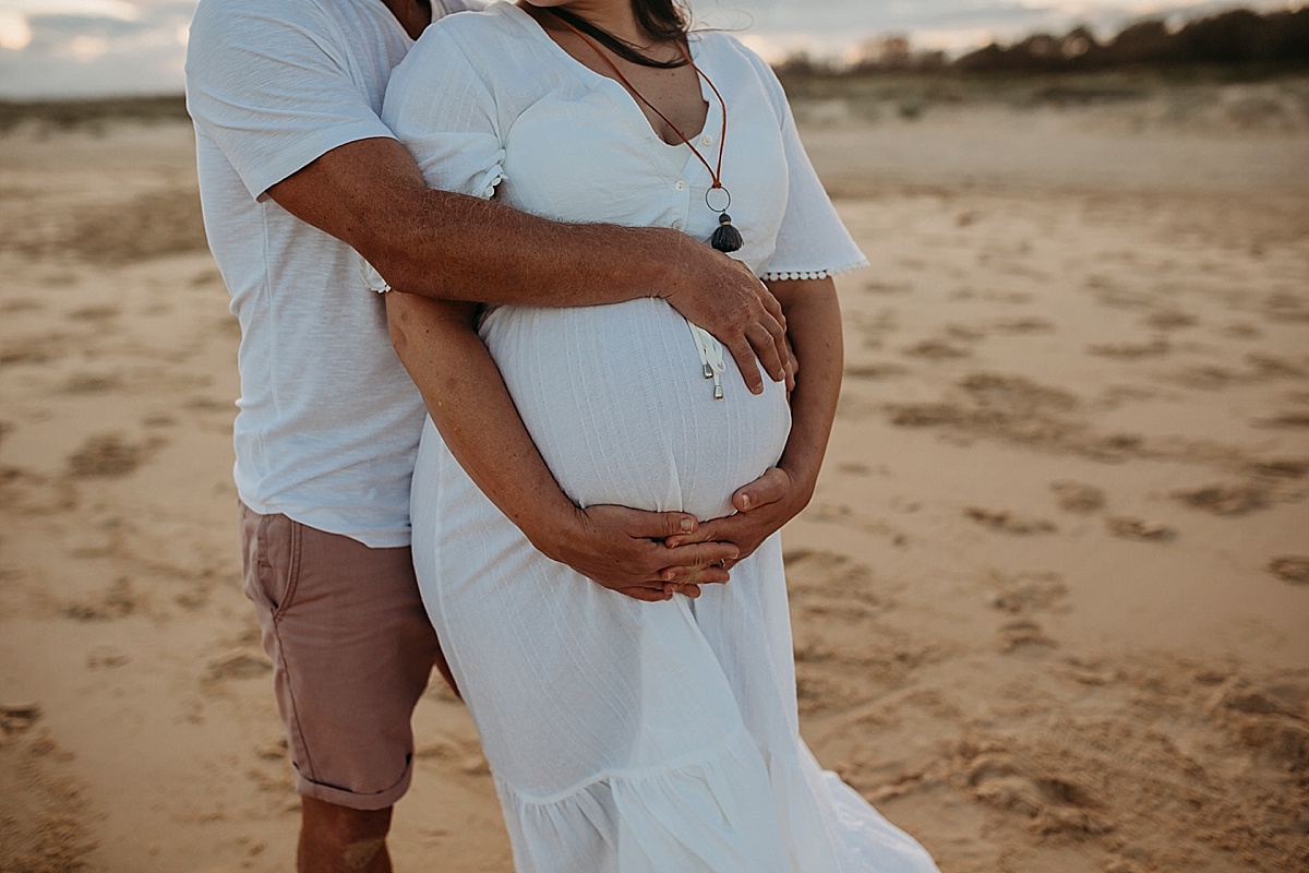 father and mothers arms wrapper around pregnant belly