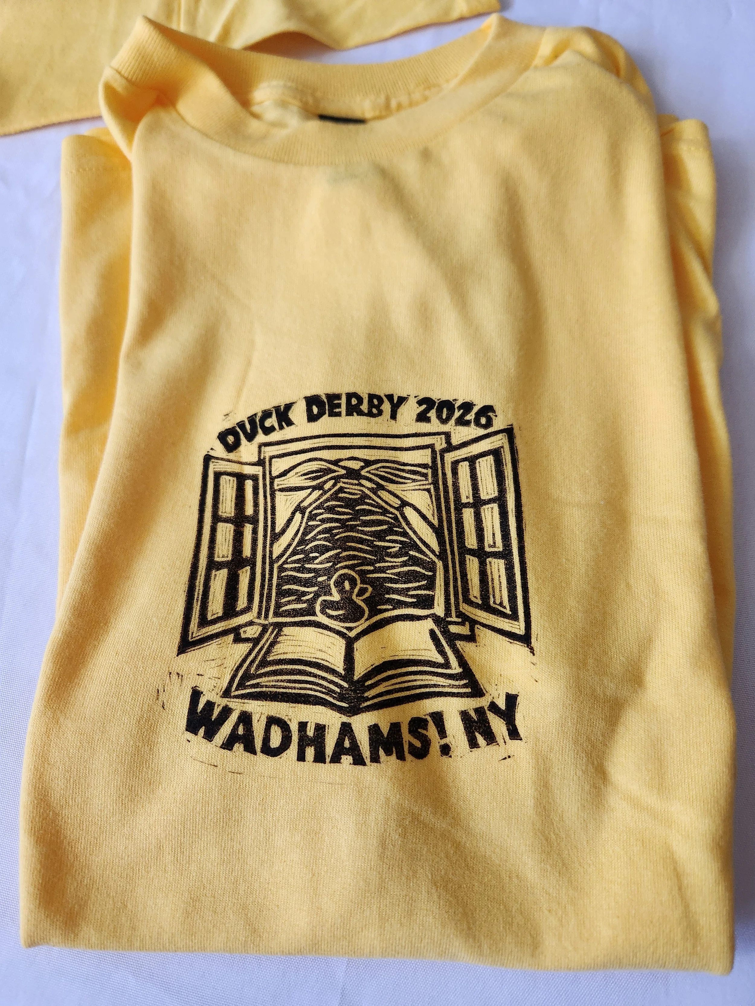 yellow tshirt with lino cut print of wadhams free library logo open window on the world with a duck and an open book Duck derby Wadhams! NY