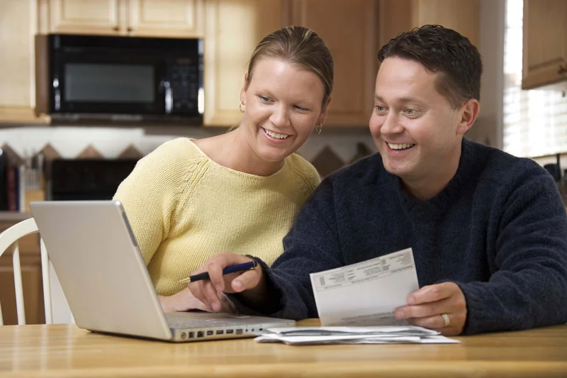 A married couple happily looking through their online bank statement on their computer.