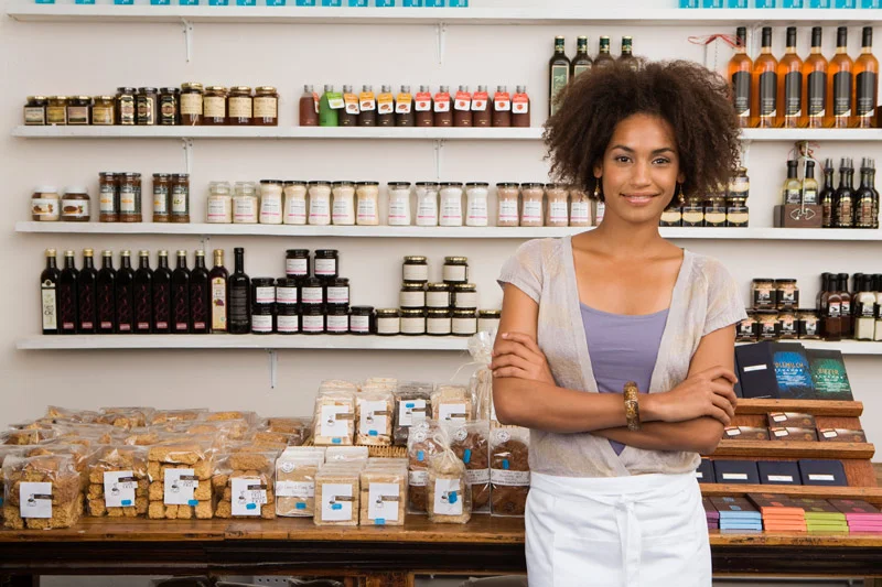 Smiling shop owner, standing in front of her fonfectionaries, oils, and chocolates.