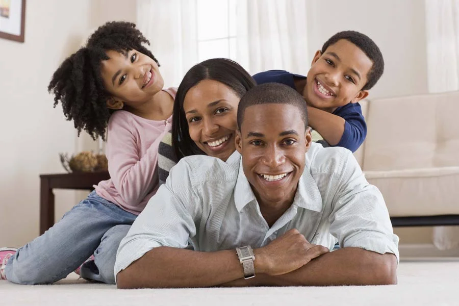 Happy family posing for a photo, lying on their carpeted living room floor.