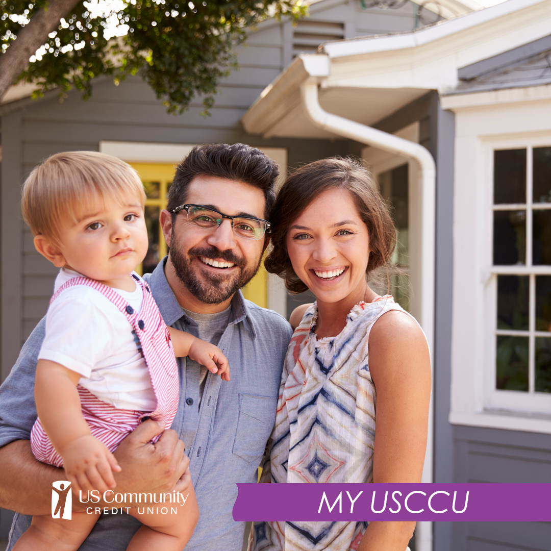 A smiling husband and wife, holding their young son, in front of their house.