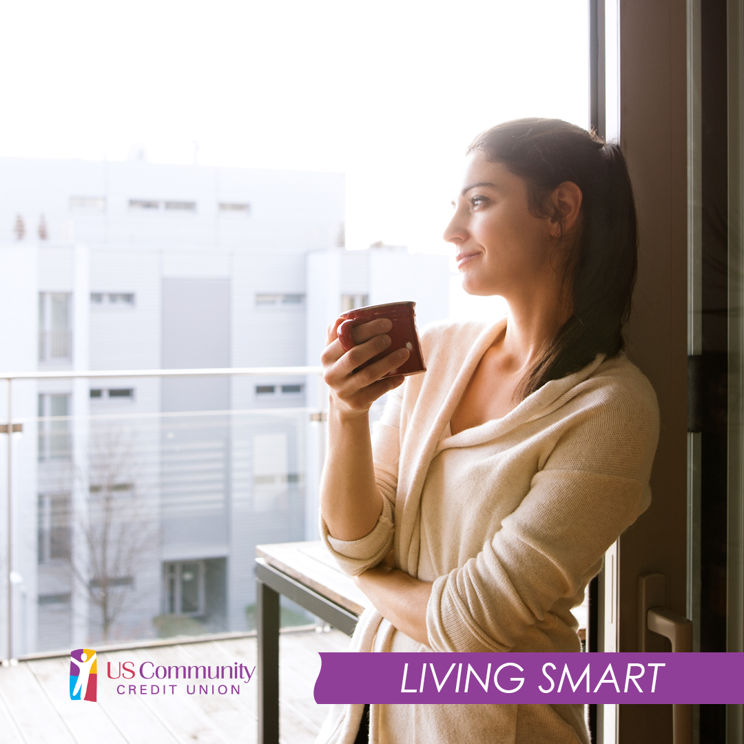 A smiling woman holding a cup of coffee, looking out the window