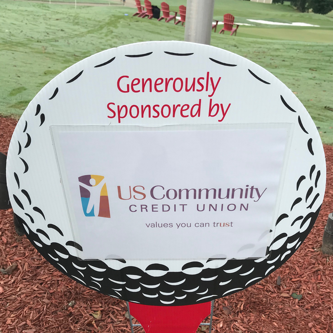A golf course sign reading “Generously Sponsored by US Community Credit Union - values you can trust”