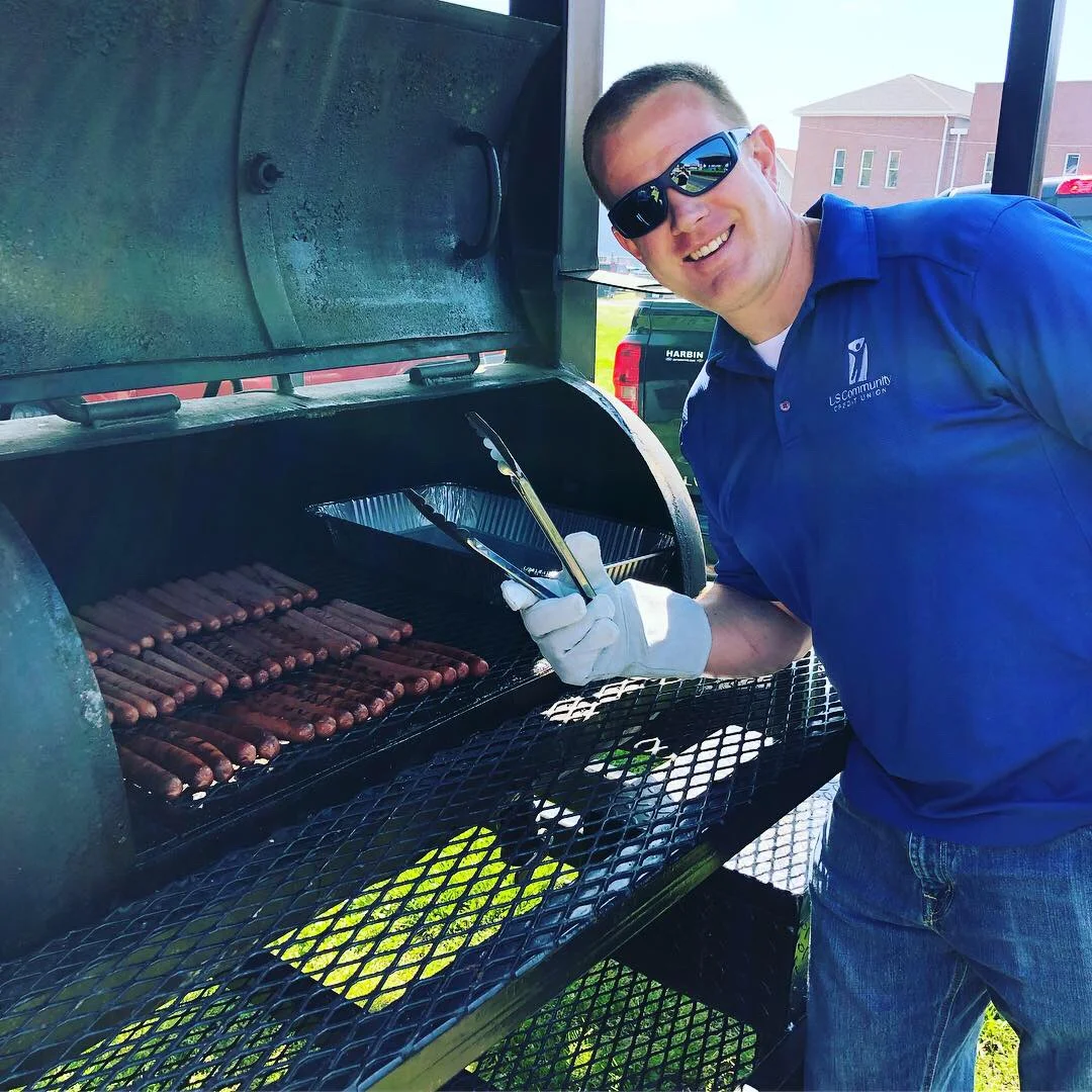 A smiling USCCU employee working the grill at a cookout