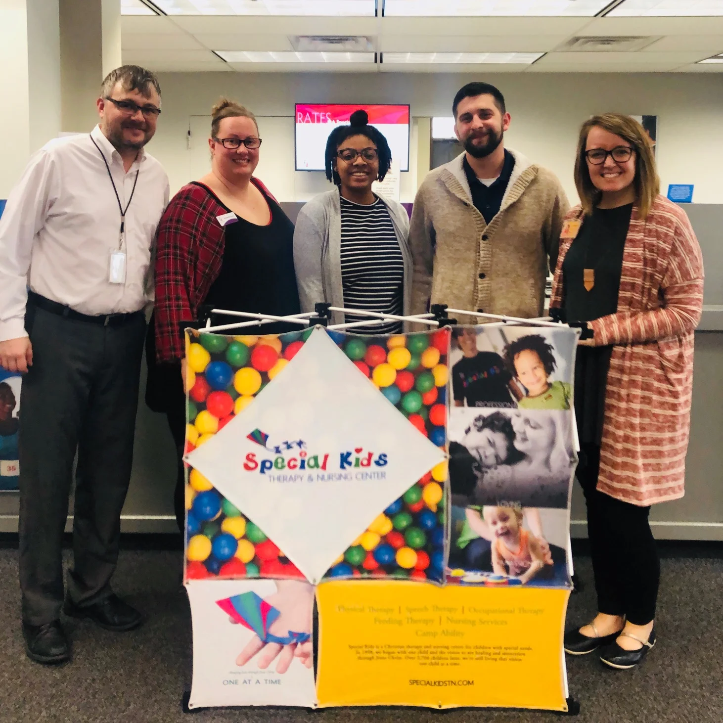 A smiling group of people standing next to a photo collage, with a sign reading “Special Kids”