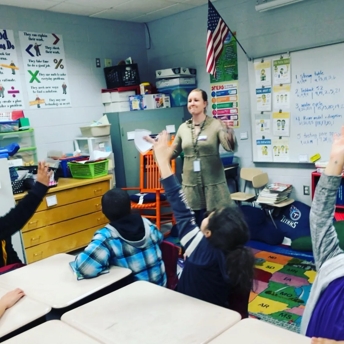 A teacher with a classroom full of children raising their hands