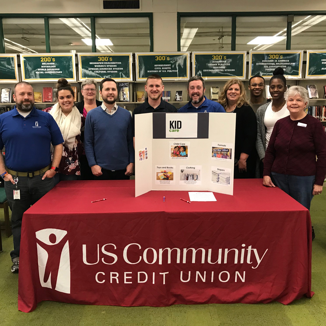 A group photo of USCCU employees in front of a table with a sign reading “US Community Credit Union”