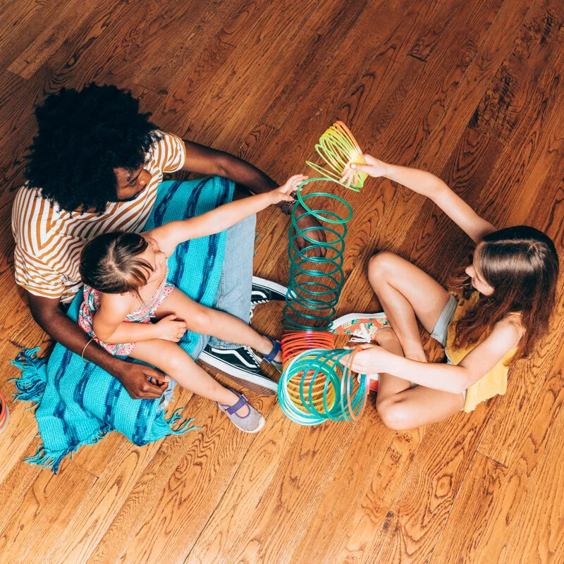 A parent and two children playing with toys while sitting on the floor.