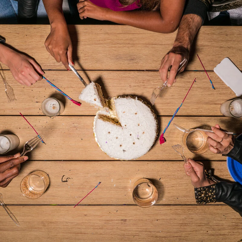 A group of friends slicing a cake and getting ready to eat.