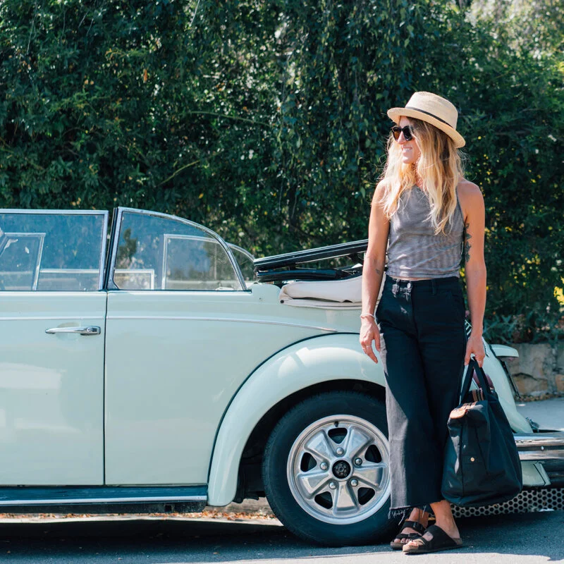 A lady wearing a hat and standing in front of an old car.