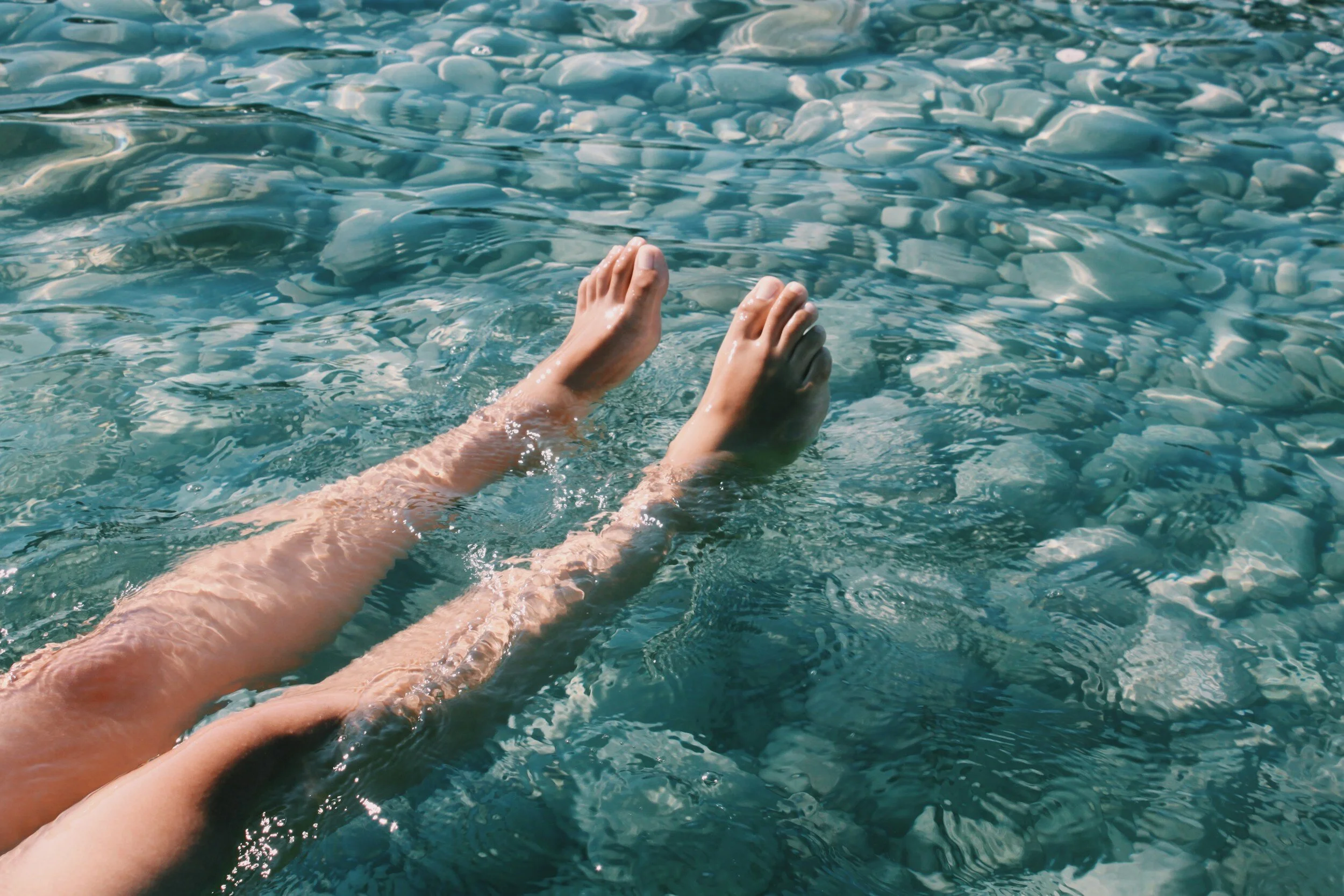 Person swimming in clear blue water, with legs and feet visible above the water surface.