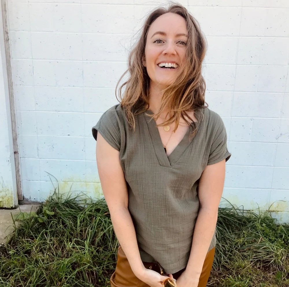 Anne, a blonde woman with wavy hair blowing in the breeze smiling at the camera.