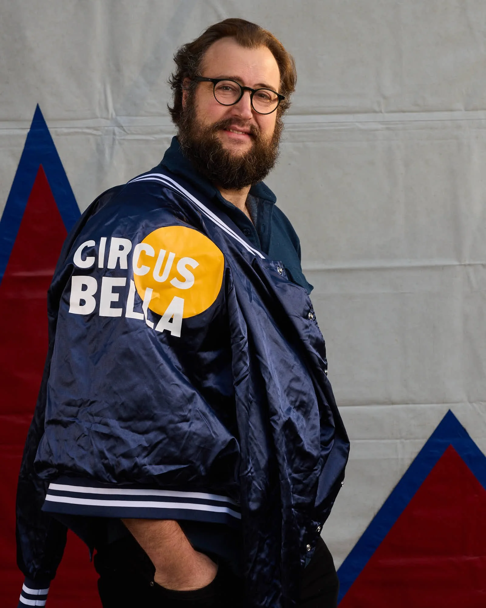 Tubaist Jonathan Seiberlich is standing with glasses and a beard, wearing a blue jacket, looking over his shoulder at the camera.
