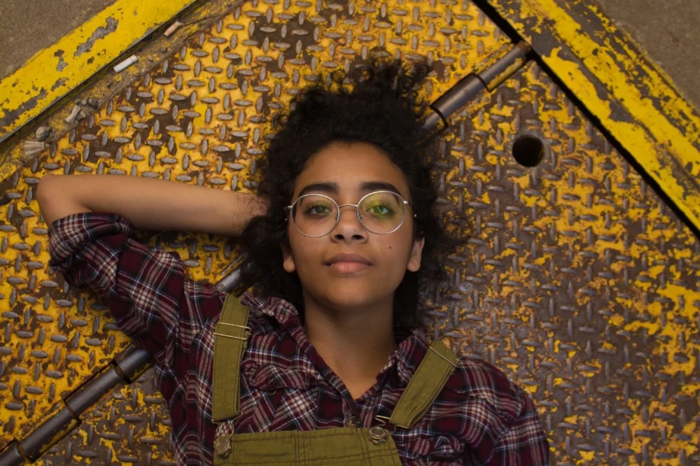 Young woman in overalls lying on a metal floor looking content. I help young people develop self-awareness and self-assurance through relational psychotherapy in Melbourne.