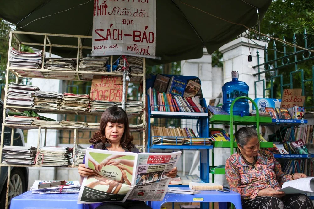 Nhiều người yêu mến, ủng hộ đã lặn lội từ nơi xa đến chỉ để biếu bà những cuốn sách, tờ báo, người thì ủng hộ cái ô, bình nước. Và cứ mỗi ngày, sạp báo của bà lại thêm một cuốn sách, thêm một tiếng cười. (Ảnh: Minh Sơn/Vietnam). Nhiều người yêu mến, ủng hộ đã lặn lội từ nơi xa đến chỉ để biếu bà những cuốn sách, tờ báo, người thì ủng hộ cái ô, bình nước. Và cứ mỗi ngày, sạp báo của bà lại thêm một cuốn sách, thêm một tiếng cười. (Ảnh: Minh Sơn/Vietnam)