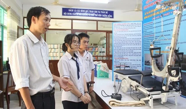 Em Nguyễn Thiện Luận cùng em gái Nguyễn Thị Bích Liên và thầy Nguyễn Văn Đồng bên chiếc ghế kéo cột sống cổ đa năng.