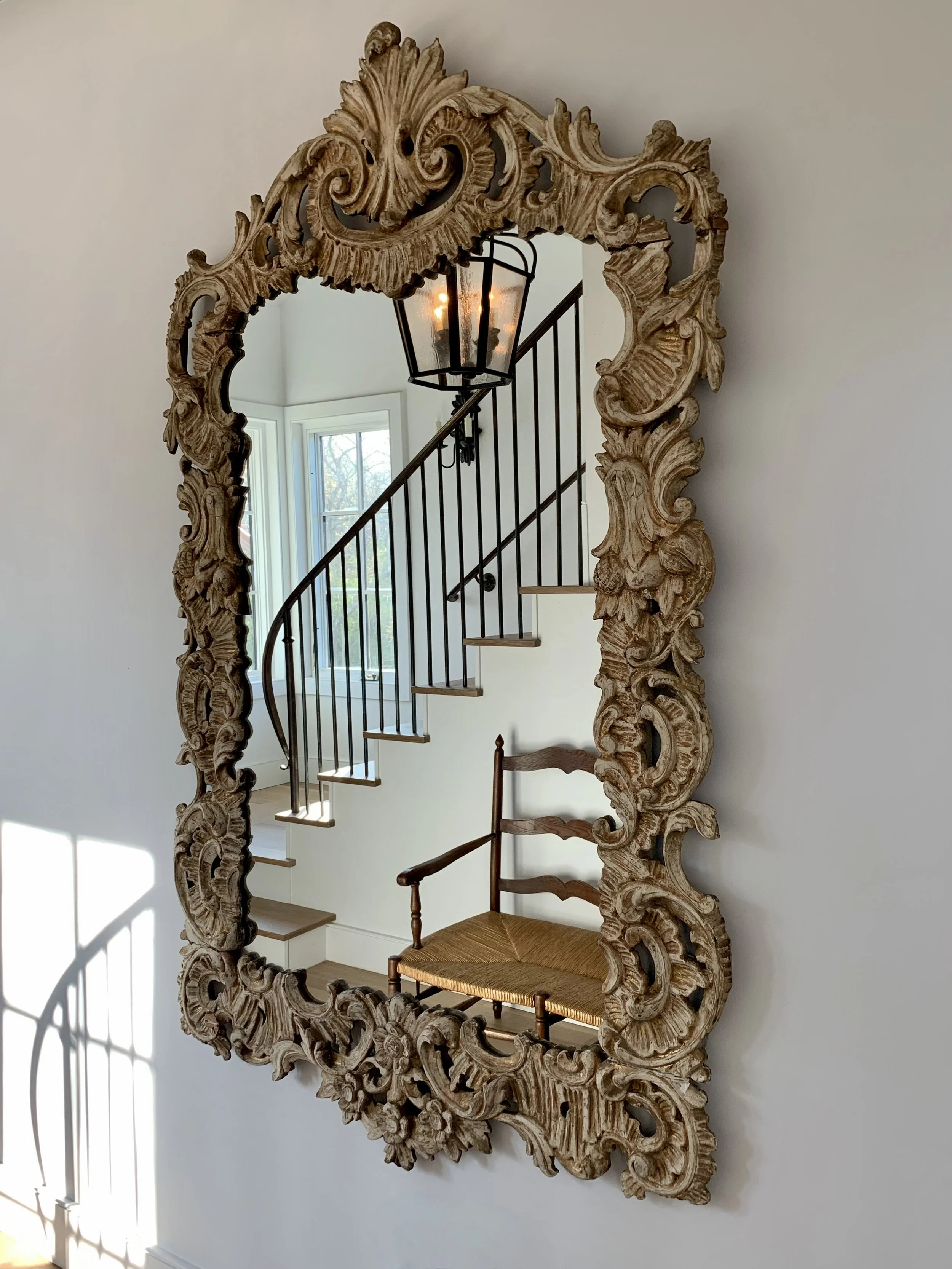 A playful Swedish baroque mirror reflects the bronze railing of the stair.