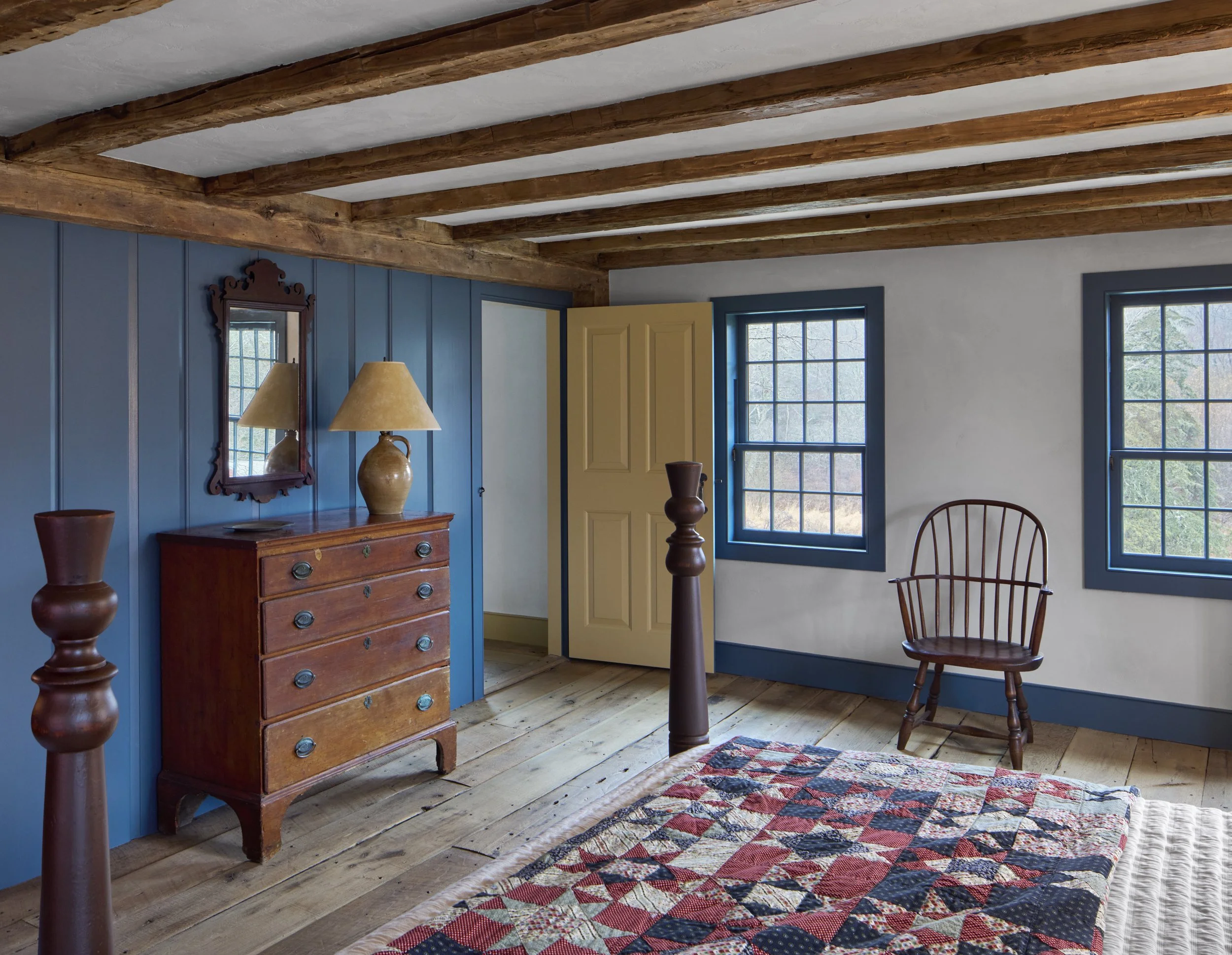  A restored bedroom in the antique house features a paneled wall and exposed ceiling beams. 