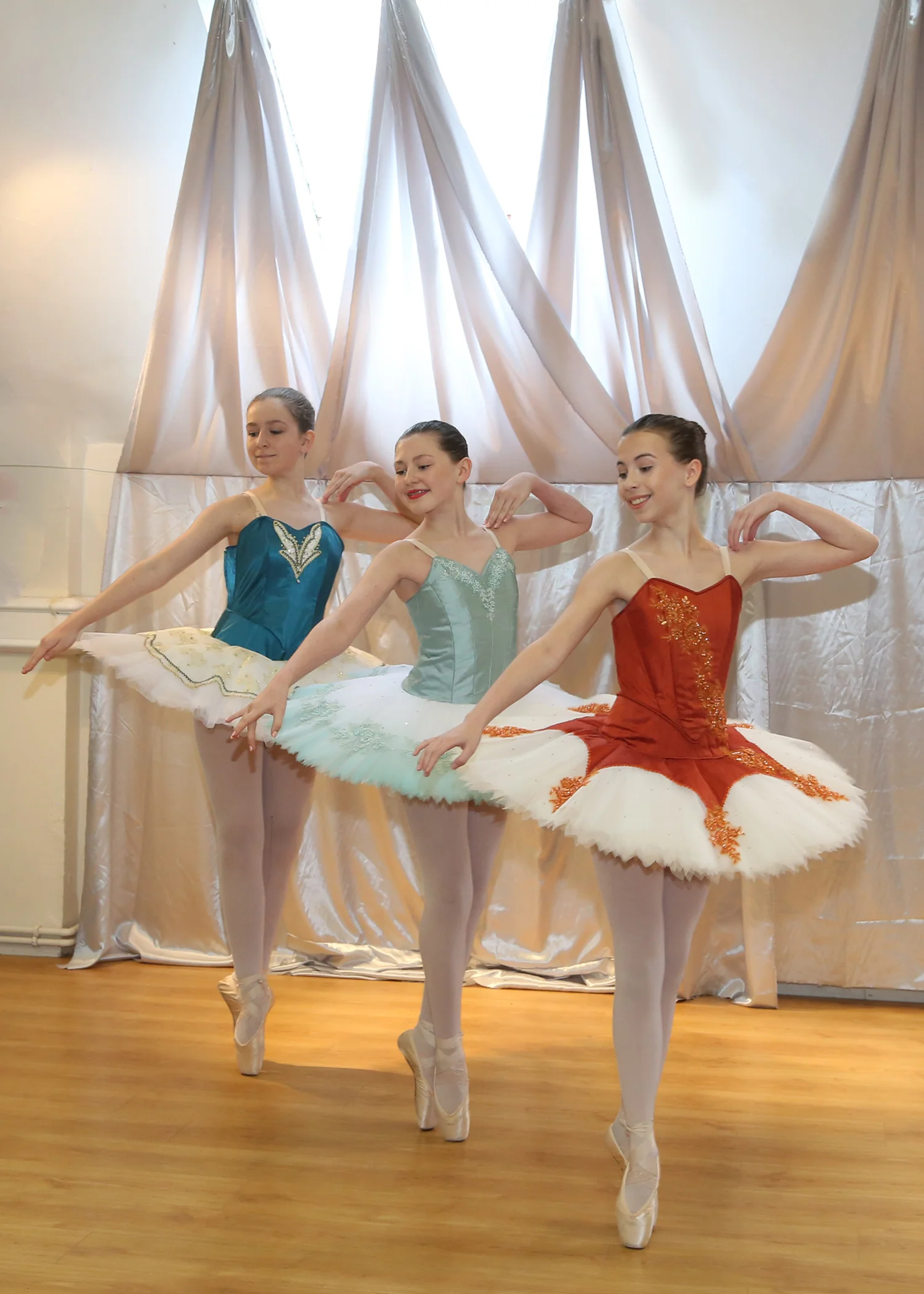 Three ballet dancers in colorful tutus practicing on stage with a golden backdrop.