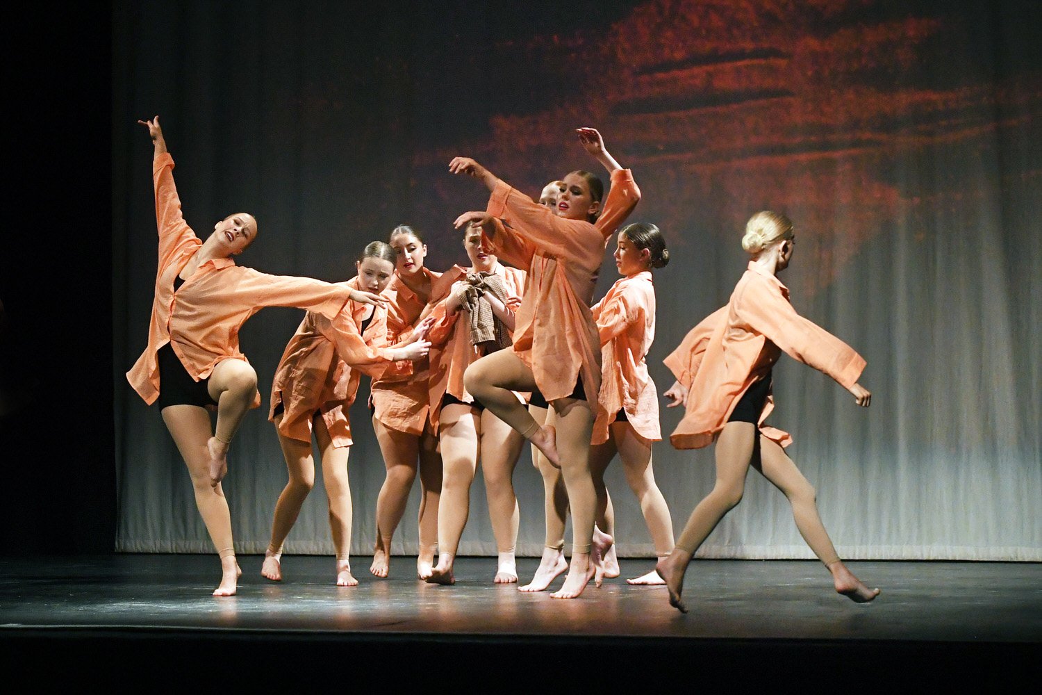 Group of ballet dancers performing on stage, wearing peach-colored shirts and black shorts.