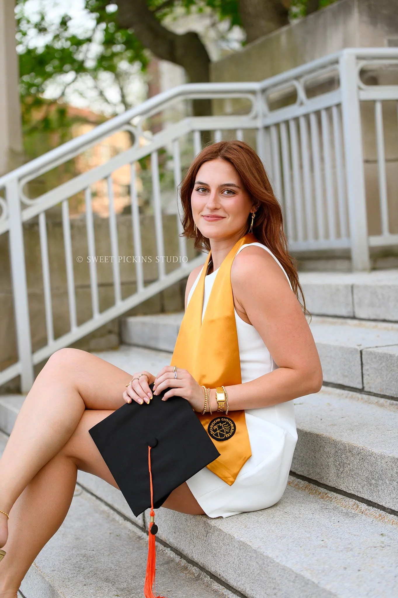 Ella’s Purdue University Graduation Photography in West Lafayette, Indiana by Sweet Pickins Studio photographer Amanda Wilson for spring graduate posing in white dress with gold stole and black cap © 2026