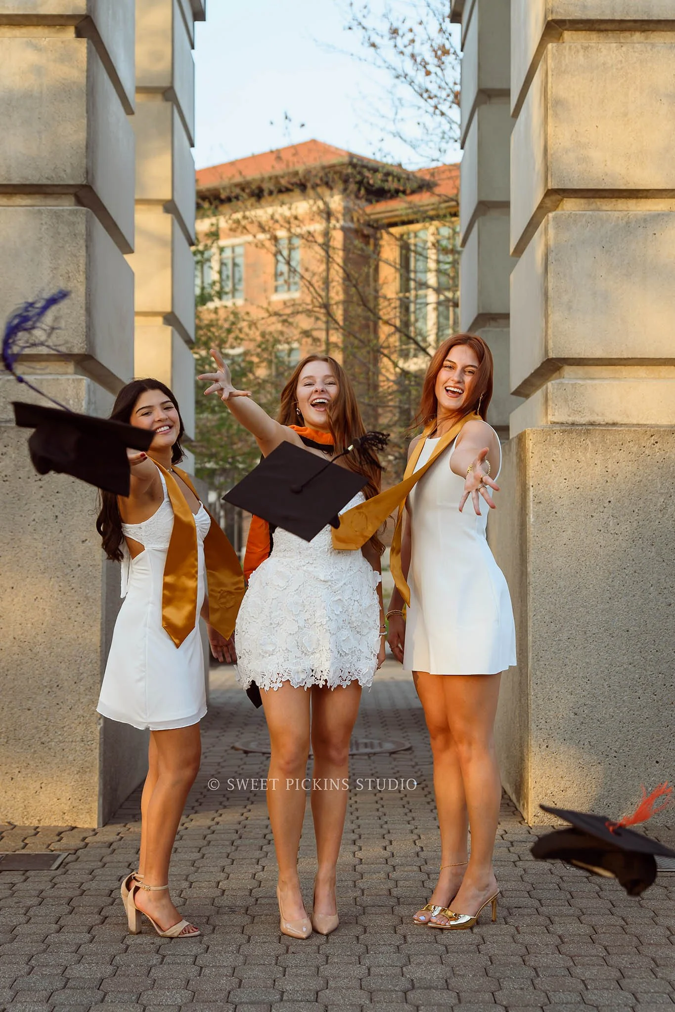 Purdue Graduation Photography for Sorority Sisters in West Lafayette, Indiana by Sweet Pickins Studio photographer Amanda Wilson for graduates posing in white dresses at Engineering arch with grad caps with tassels © 2026