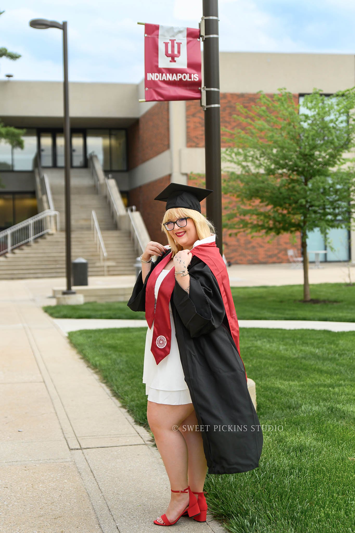 I.U. Indy Graduation Photography in Downtown Indianapolis, Indiana with class of 2026 grad wearing cap and gown holding flag by Sweet Pickins Studio senior photographer Amanda Wilson ©