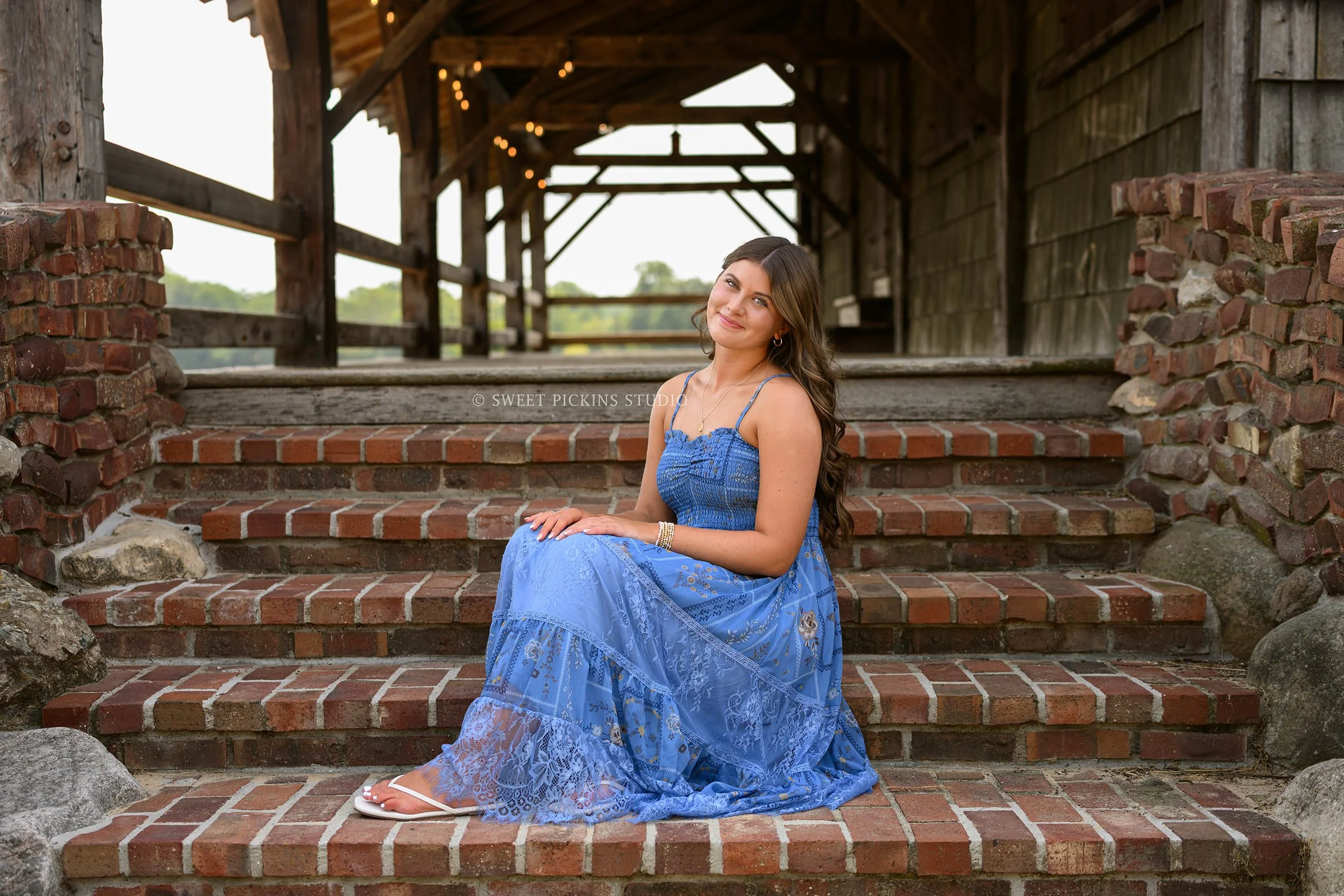 Zionsville, Indiana Senior Photography at Traders Point Creamery with class of 2027 senior girl posing in blue sun dress on brick steps of old barn by Sweet Pickins Studio senior photographer Amanda Wilson ©