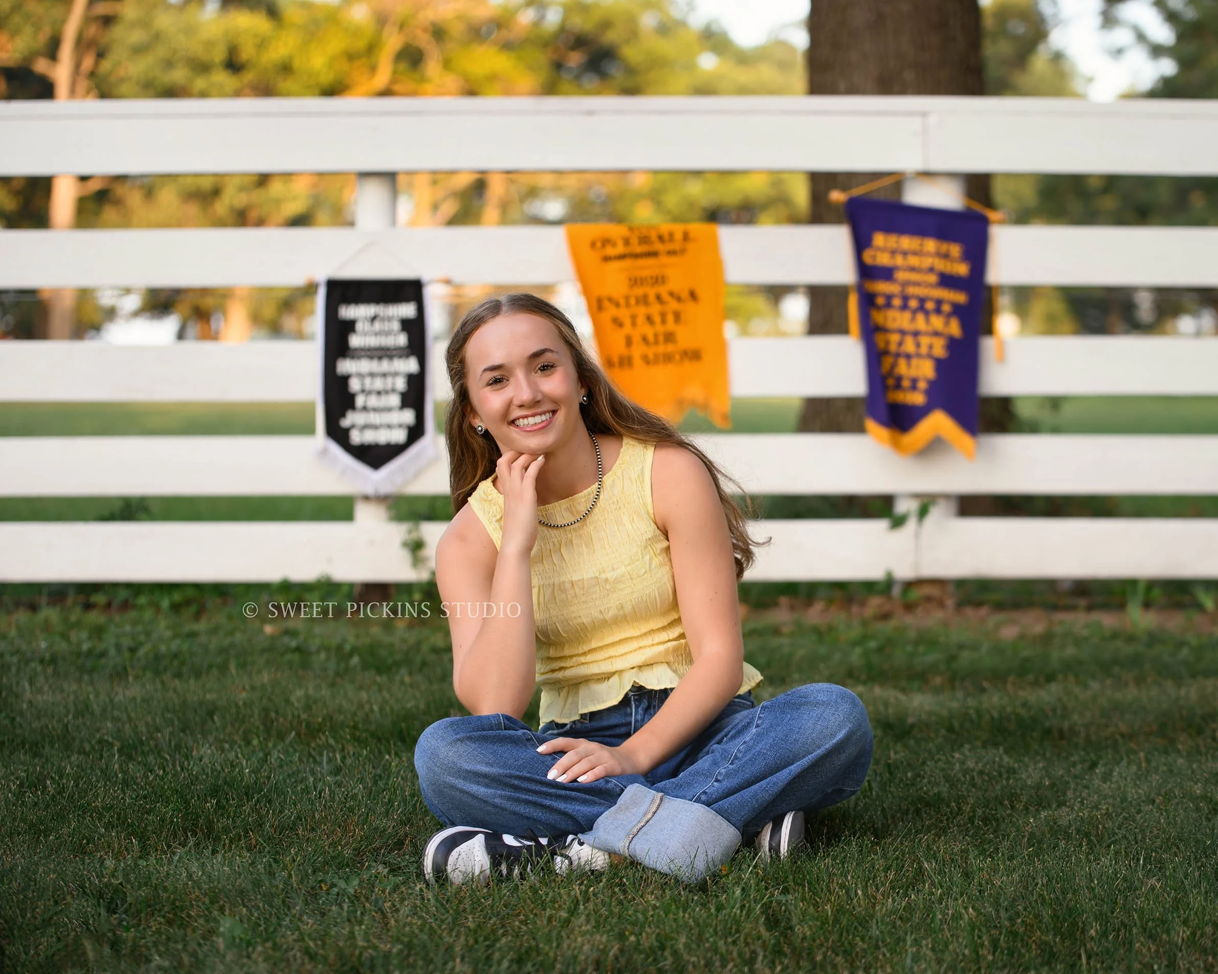 Natalie’s Lowell, Indiana 4-H Senior Photography for class of 2027 senior girl posing with 4-H banners on fence at family farm by Sweet Pickins Studio senior photographer Amanda Wilson ©
