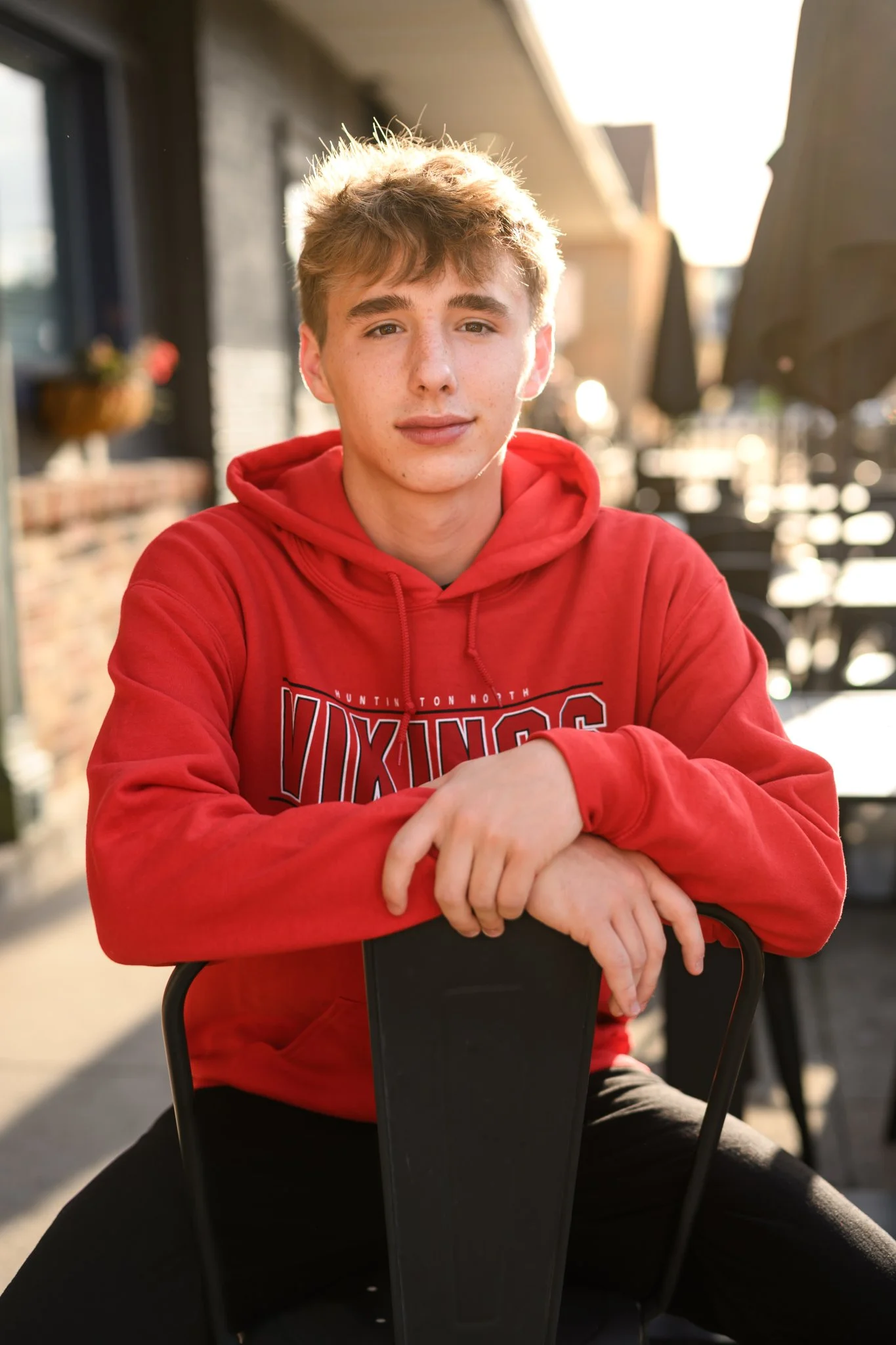 Huntington, Indiana Urban Senior Guy Photography for Huntington North Class of 2027 Senior  BOSTAN posing on chair in urban downtown streets wearing red school hoodie by Sweet Pickins Studio senior photographer Amanda Wilson ©
