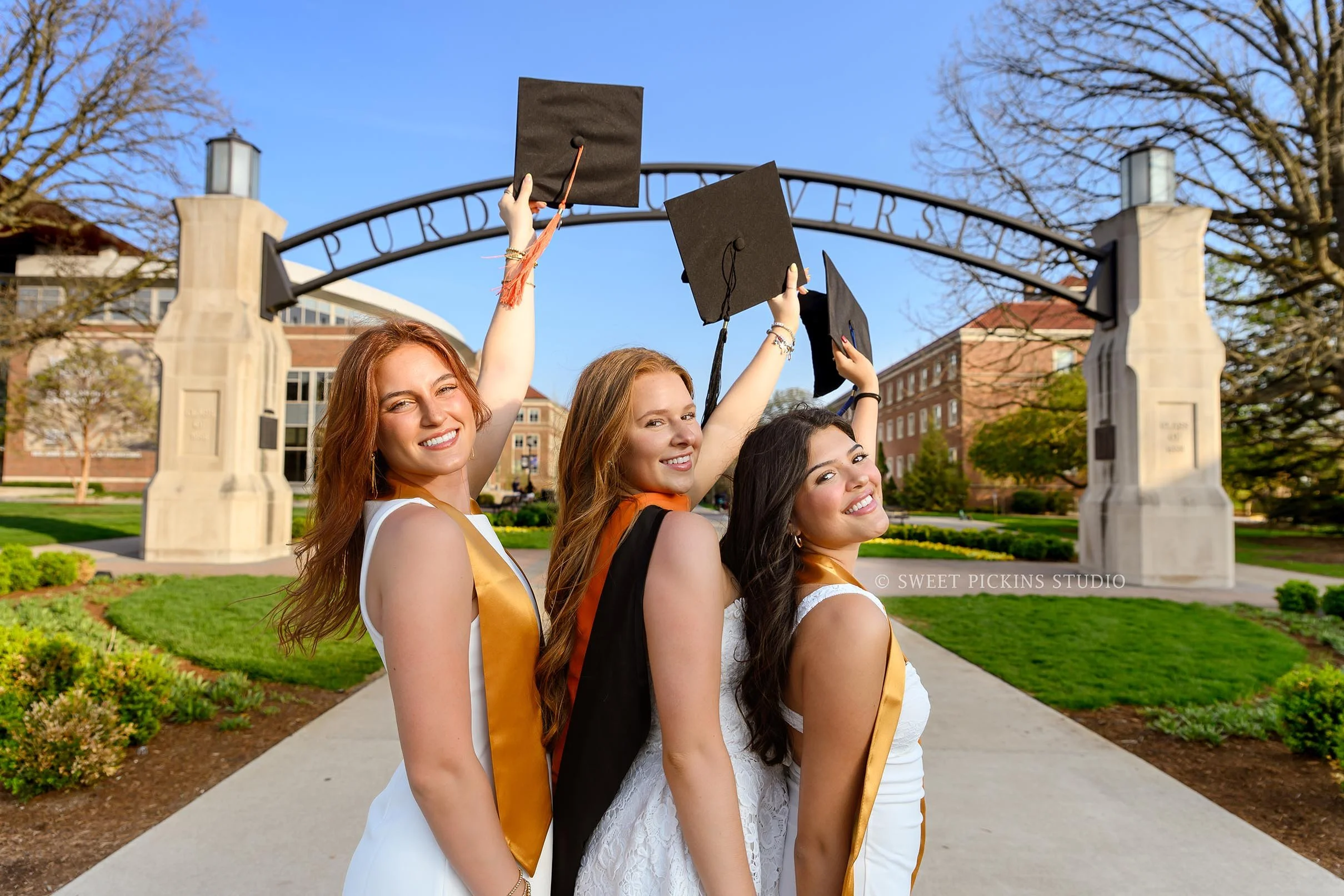 Purdue Graduation Photography for Sorority Sisters in West Lafayette, Indiana by Sweet Pickins Studio photographer Amanda Wilson for graduates posing in white dresses at Engineering arch with grad caps with tassels © 2026