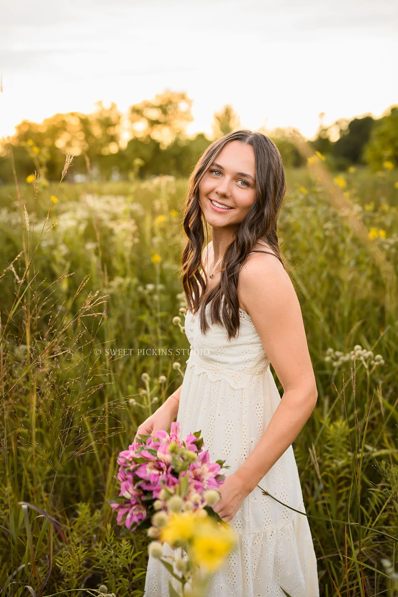 Sophie’s Carmel, Indiana Senior Photography by Sweet Pickins Studio senior photographer Amanda Wilson for class of 2027 Senior girl walking in flower field in cream maxi dress at sunset ©