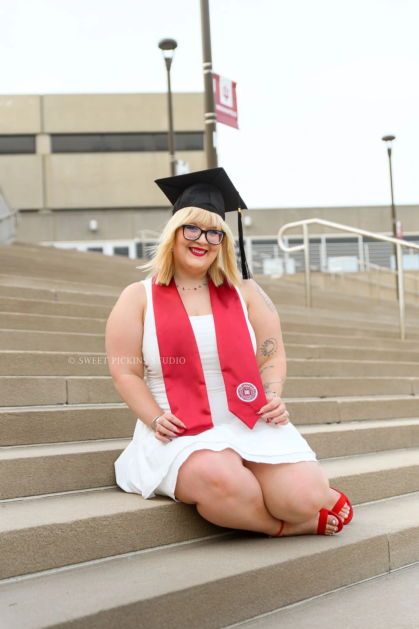 Indiana Univ at Indianapolis Graduation Photoshoot in Downtown Indianapolis, Indiana with class of 2026 grad wearing white dress and red heels on steps by Sweet Pickins Studio senior photographer Amanda Wilson ©