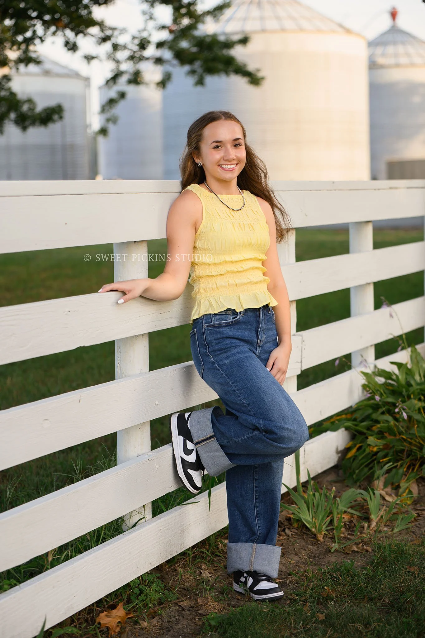 Natalie’s Lowell, Indiana Farm Senior Photography for class of 2027 senior girl posing on white fence with grain bins by Sweet Pickins Studio senior photographer Amanda Wilson ©