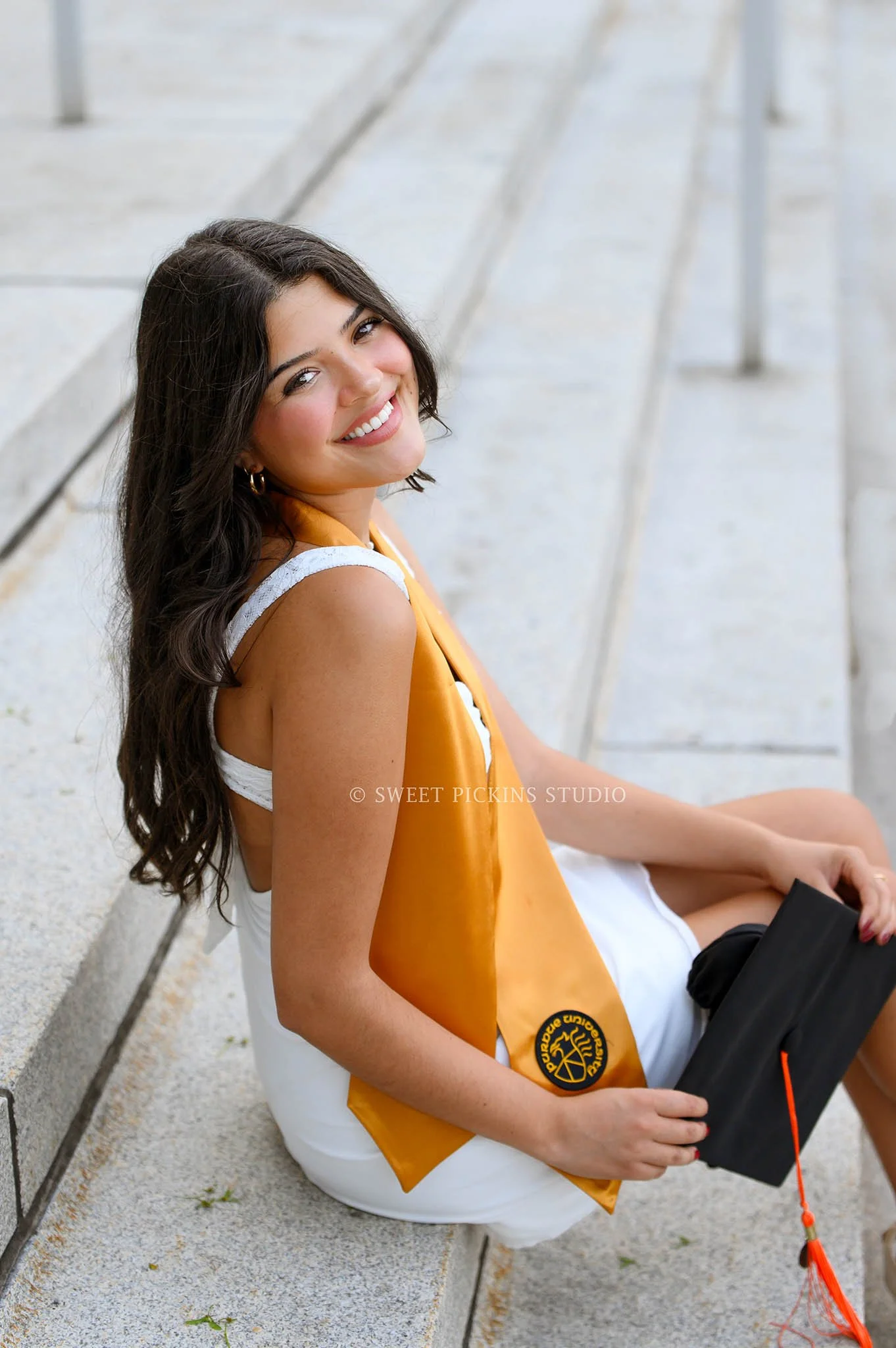 Maria’s Purdue University Graduation Portraits in West Lafayette, Indiana by Sweet Pickins Studio photographer Amanda Wilson for spring graduate posing in white dress at Hovde Hall with grad cap and tassel © 2026