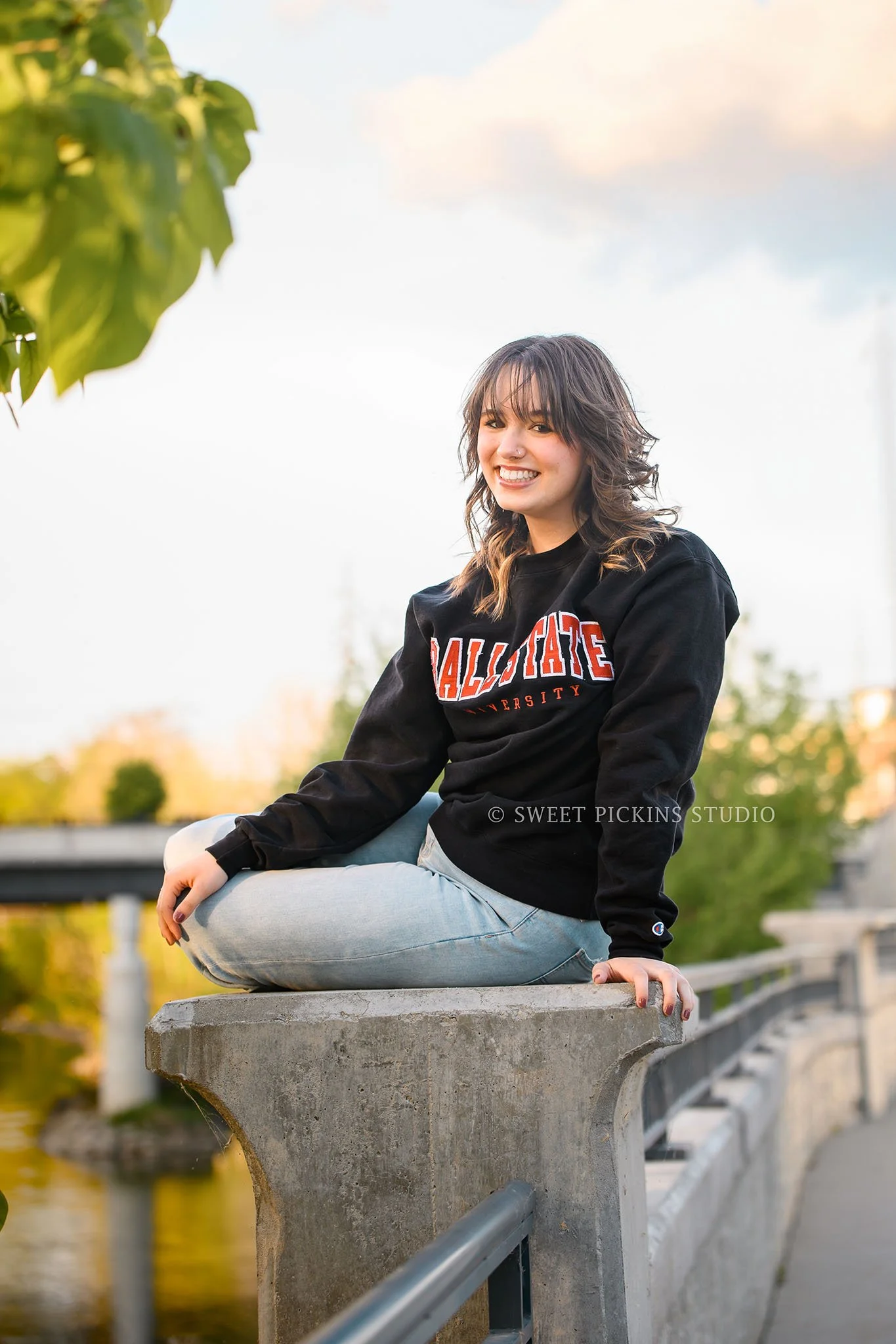 Hailee | Noblesville High School Graduation Photography in Cap and Gown at river walk wearing college sweatshirt by Sweet Pickins Studio senior photographer Amanda Wilson ©